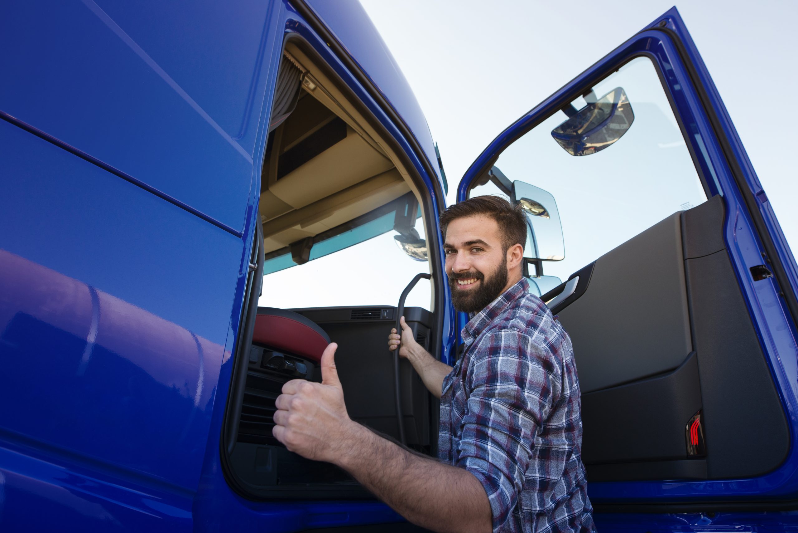 Professional truck driver entering his truck long vehicle and holding thumbs up. Loving his job.